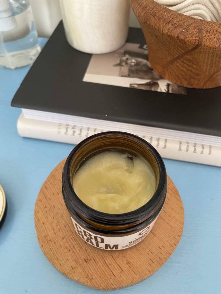 An open canister of 8Labs 500mg Full Spectrum CBD Balm sits on a blue counter, showing the creamy balm inside.